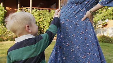 Little boy rubbing his pregnant mom's belly outdoor