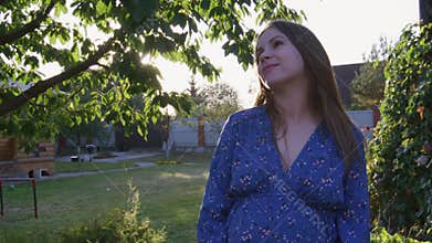 Beautiful pregnant woman enjoying fresh air at sunset rays on the backyard