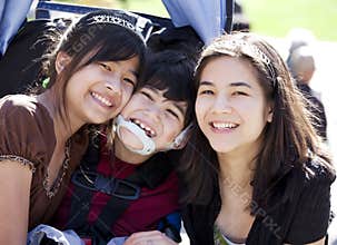 Disabled boy in wheelchair surrounded by big sisters, smiling