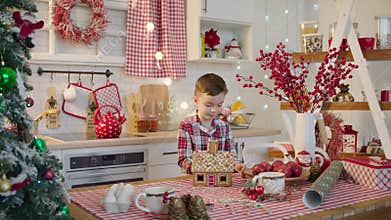 Cute boy decorating gingerbread house with topping and icing at the kitchen