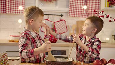 Cute boys making gingerbread dough together at the kitchen on Christmas eve