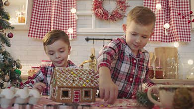 Cute boys decorating gingerbread house with topping and icing at the kitchen