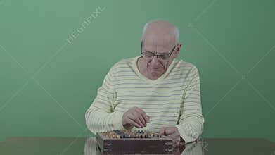Old accountant in glasses counts on vintage abacus on wooden table isolated on green