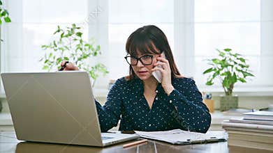 Middle-aged business woman talking on mobile phone sitting at desk with computer