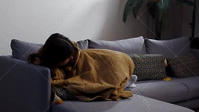 A brunette woman lies on the couch wrapped in a blanket. Tired young woman wraps herself in a blanket and falls asleep