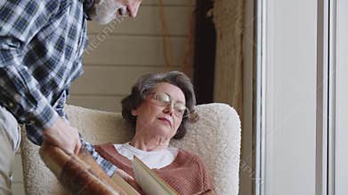 A careful gray-haired husband covers his sleeping wife with a cozy blanket. The elderly lady fell asleep in an easy