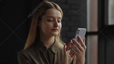 A young woman quickly taps on the smartphone screen. A long-haired blonde woman is chatting with a friend via a
