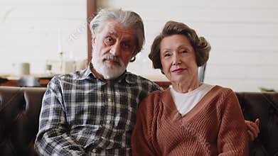 Loving mature married family couple looking at camera. Beautiful elderly couple hugging each other sitting on sofa at
