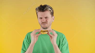 The young guy first sniffs and then bites off the cake and shakes his head disapprovingly. A man in a green t-shirt is