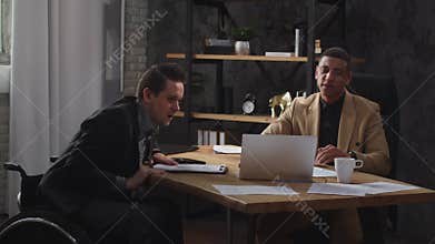 Two men in business suits are looking at a laptop screen and discussing something animatedly. Office workers watch