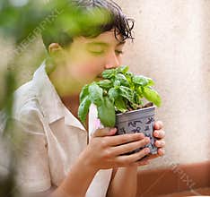 10-year-old boy smelling basil plant in his small vegetable garden