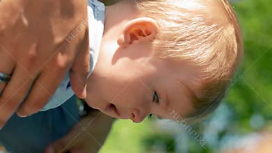 Vertical of Baby boy sits pouting cheeks near father on picnic closeup