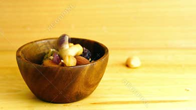 Breakfast mix nuts and dry tropical fruit falling into wooden bowl.