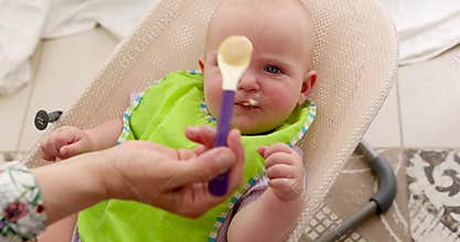 Adorable cute baby seated in a high chair with a green bib, relaxing comfortably at home
