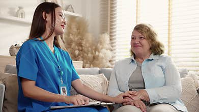 Young asian caregiver woman or doctor sitting on sofa encourage and care senior in living room at home.