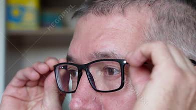 A man puts on glasses with black plastic frames to see better