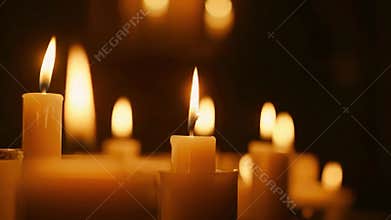 Close up of several lit candles with soft glowing light in a dark room