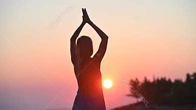Footage of a young woman in summer dress meditating at warm sunrise