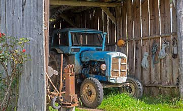 Old blue tractor in a wooden garage in a rural area