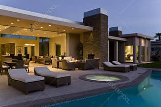 House With Sunloungers On Patio By Pool At Dusk