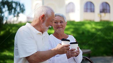 Cheerful married senior couple spending time together in green park, holding coffee cups and enjoying each other company