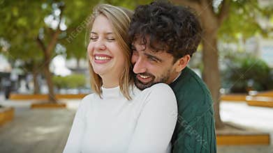 A happy couple embraces in a sunny park with lush green trees in the background
