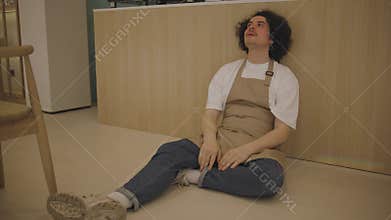 A guy waiter, tired from overwork, sit on the floor in a cafe next to the bar counter and upset. Frustrated man sits on