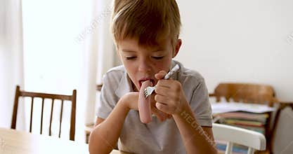 Young boy struggling to eat a sausage stubbornly stuck on his fork
