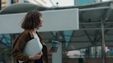 Charming Girl After Work Holding Coffee And Laptop Walking and Enjoying her Coffee.