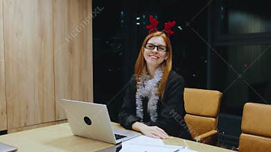 A cheerful woman wearing reindeer antlers is seen in a modern office environment, embodying a lively atmosphere that