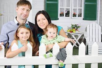 Father, mother, baby and daughter stand next to white fence