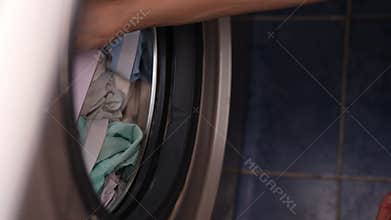 Close-up top view of unrecognizable man loading garment into washing machine tank during daily chore of laundry and