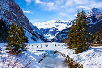 Visitors skating on frozen Lake Louise in Winter against the backdrop of the stunning Victoria Glacier
