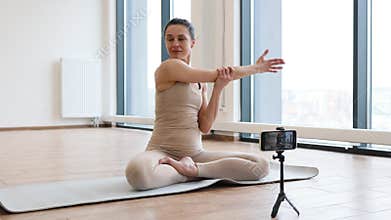 Adult doing padmasana exercise on mat shooting video content on smartphone.