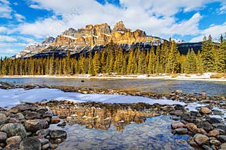 Winter snow along the banks of the Bow River in Banff with snow-melted puddle reflection of majestic Castle Mountain