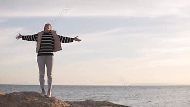 Happy woman raising her hands up against the background of mountains and sea