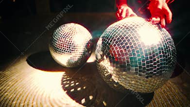 Close-up shot of female hands touching holding rotatimg silver shiny disco ball glowing rays light spot black dark room