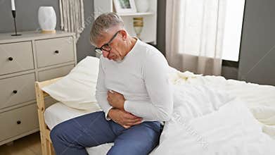 Middle-aged, grey-haired man feeling ill, wearing pyjamas, hand on aching stomach, suffering from painful illness in the solitude