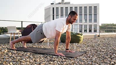 Young smiling sports man doing morning exercises on roof of modern house.