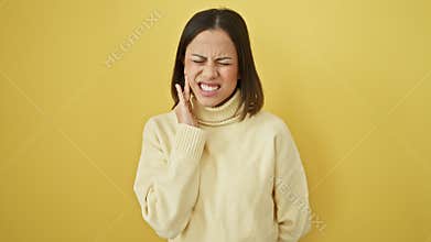 Young hispanic woman in pain - portrait of a beautiful female feeling dental ache, touching aching tooth on yellow isolated
