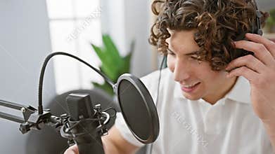 Handsome young man with curly hair adjusting headphones while podcasting in a modern studio