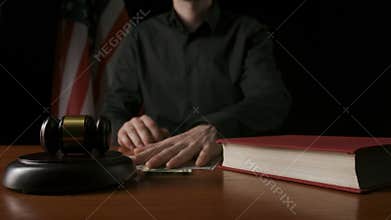 Law and justice. Male sitting at the desk with wooden hammer and law book, USA flag at the background. Man judge in the