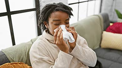 A young african american woman with dreadlocks blows her nose on a sofa indoors, suggesting illness or allergies
