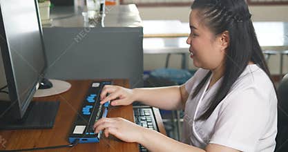 Asian woman with blindness disability using computer with refreshable braille display or braille terminal a technology assistive