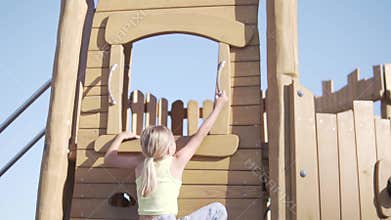 A girl climbs up on a wooden playground, slow motion filming
