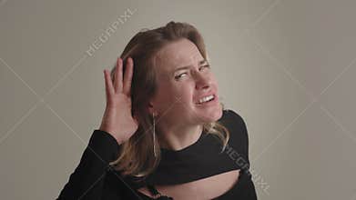 A young American or European blonde woman with bad hearing tilts head forward, holds hand on ear and asks question what