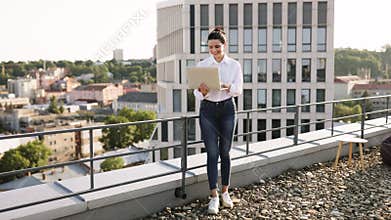 Young woman working on rooftop with laptop in urban setting