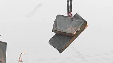 Video 4k. Crane lifting concrete blocks against a grey sky backdrop.