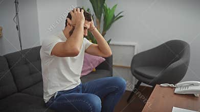 Stressed middle age man at home, clutching his aching head in hands, battling intense migraine pain and stress, while wearing a