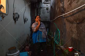 A pensive woman standing in a narrow alleyway while wearing a grey shawl